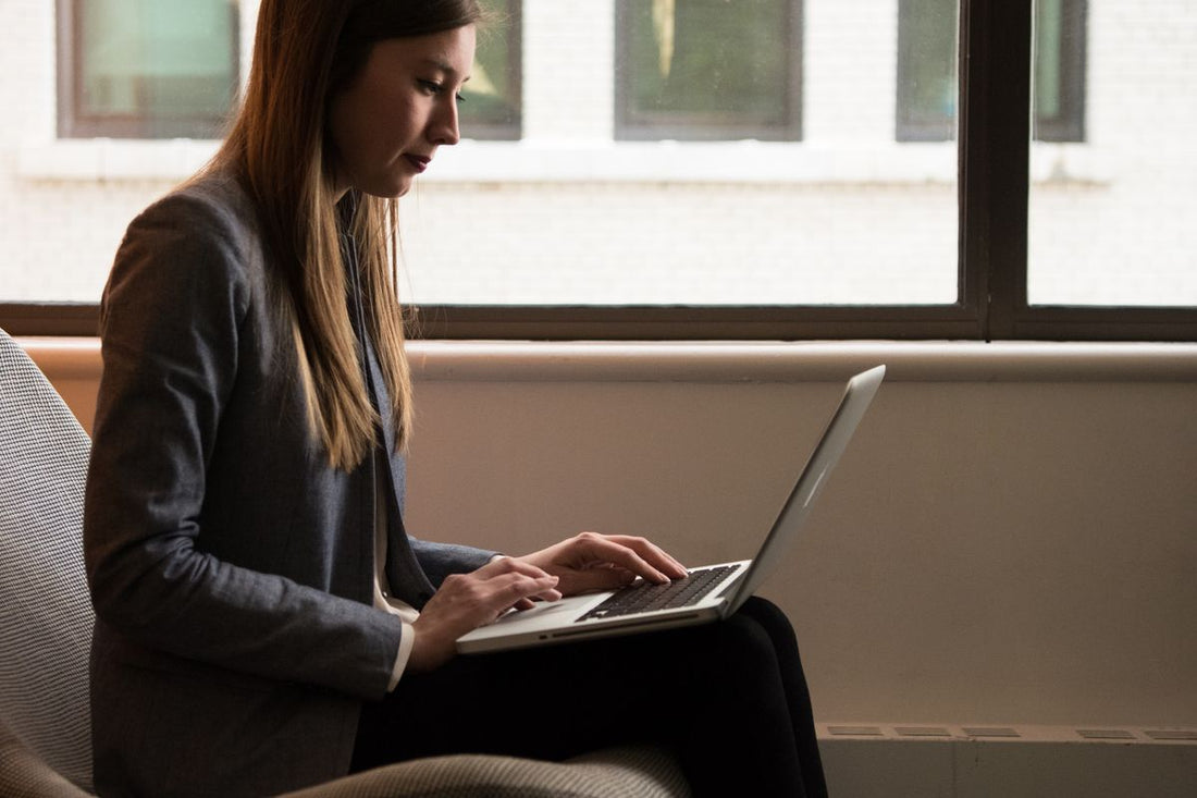 Woman sitting upright with a laptop by a window, posture-friendly position