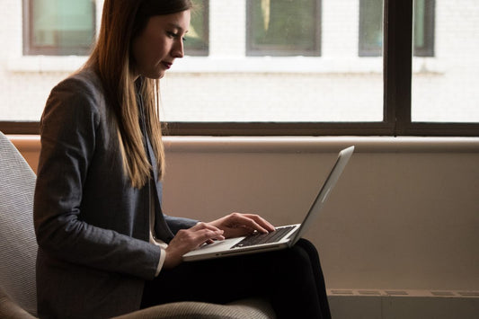 Woman sitting upright with a laptop by a window, posture-friendly position